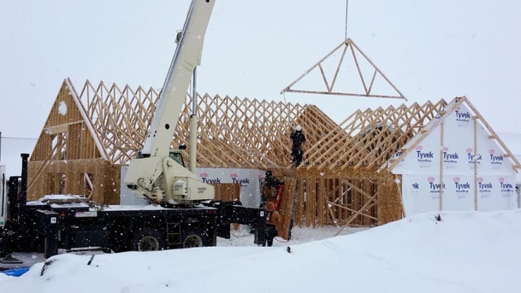 Crane dropping roof rafter on new custom home in snow