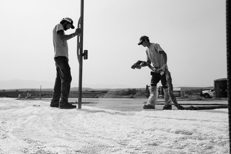 Black and white image of two builders working on foundation for new construction with excavator in back