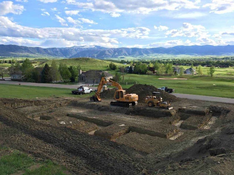 View of new construction home site in progress with excavator in front of scenic Wyoming mountains